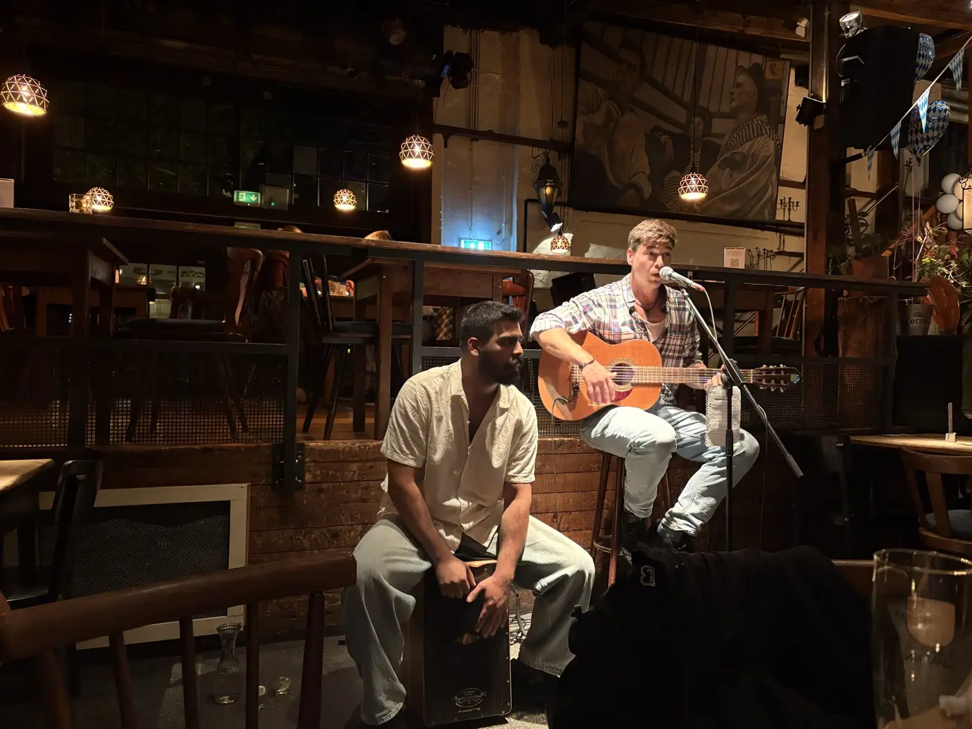 Die Musiker spielen abends in einer Bar, einer am Cajón, einer mit Gitarre am Mikrofon
